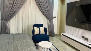 A modern bedroom with a large bed, a blue armchair, a small round table, and a TV mounted on the wall. - Stylish 2-Bed Luxury Apartment in Ikeja GRA – 24/7 Power & Comfort (Lagos)