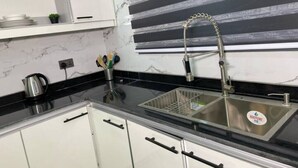 A kitchen with a black countertop, white cabinets, a stainless steel sink, and a marble backsplash. - Stylish 2-Bed Luxury Apartment in Ikeja GRA – 24/7 Power & Comfort (Lagos)