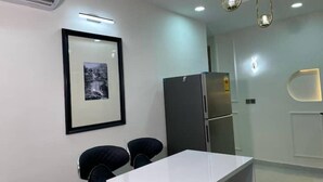 A modern kitchen with a white countertop, two black chairs, a framed picture on the wall, and a stainless steel refrigerator. - Stylish 2-Bed Luxury Apartment in Ikeja GRA – 24/7 Power & Comfort (Lagos)