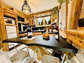 Une cuisine rustique avec des meubles en bois, un plan de travail noir et un coin repas avec des chaises blanches.