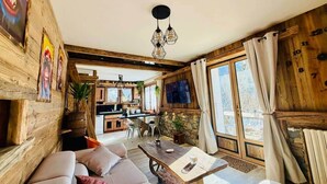 Un ambiente rustico con zona pranzo in legno, una poltrona e una cucina sullo sfondo.