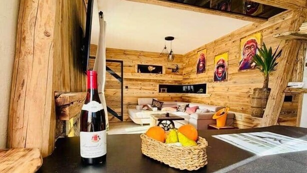 Un accogliente soggiorno con pareti in legno, un tavolo nero, una bottiglia di vino e un cesto di frutta.
