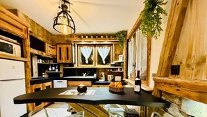 Una cucina compatta con mobili in legno, un piano di lavoro nero e un muro in pietra. È presente una piccola zona pranzo con sedie bianche e un tavolo.