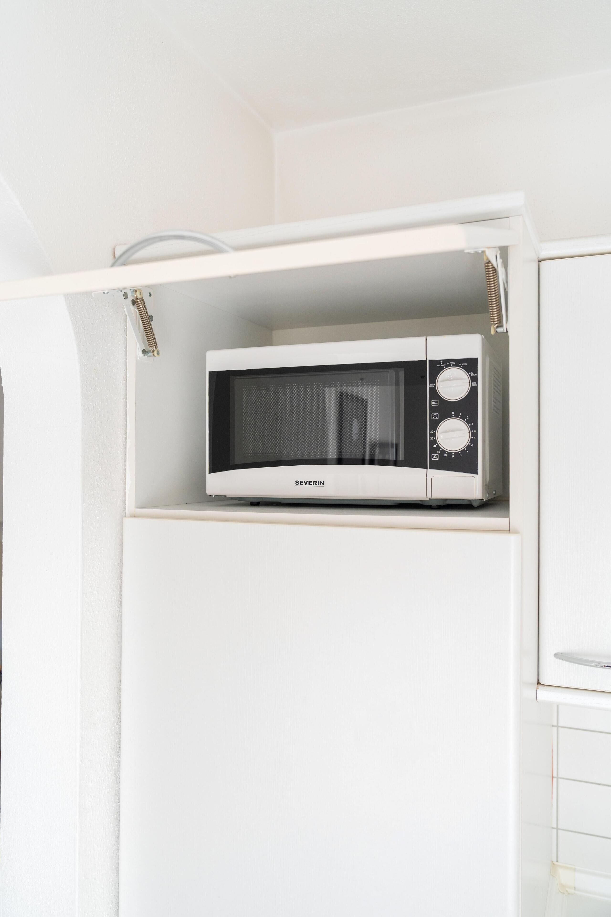 A white microwave on a shelf in a white kitchen cabinet.