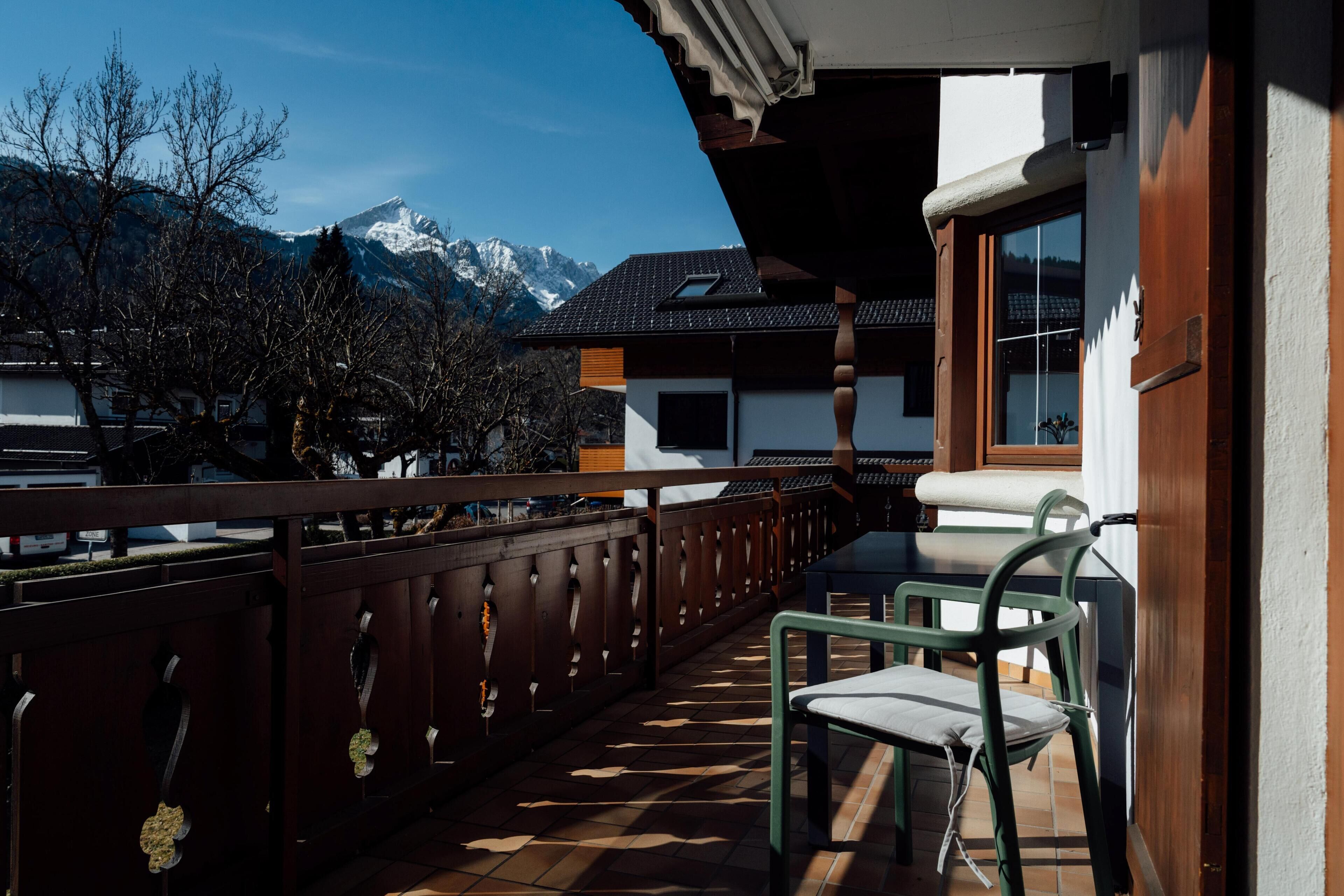 Un balcon offrant une vue sur des montagnes enneigées, une clôture en bois et une chaise.