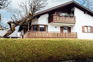 Eine zweistöckige Chalet mit Balkon, Holzzaun und gepflegtem Heckenstreifen.