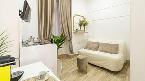 A small, modern room with a white sofa, a small table with a coffee maker, a plant, and a mirror on the wall. - Mega Random By Dimorra (Naples)