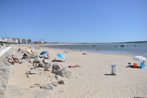 A sandy beach with people sunbathing and swimming, a clear sky, and boats in the water. - Casa do Facho – Stylish Two-Bedroom Apartment Overlooking the Atlantic (São Martinho do Porto)
