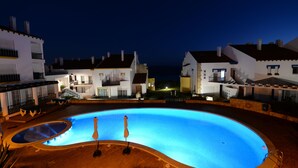 Una piscina con una zona hundida, rodeada de edificios con balcones y un muro de piedra.