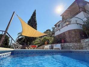A swimming pool with a sunshade, stone wall, and a white building with a balcony.
