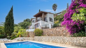 A two-story house with a stone wall and a swimming pool in the foreground.