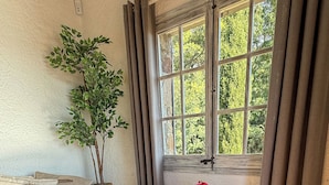 A cozy room with a wooden floor, a white sofa, a small round table with a vase of red flowers, and a potted plant.