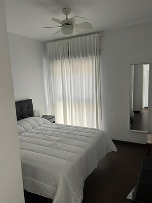 A bedroom with a bed, a ceiling fan, a nightstand, a mirror, and a window with curtains. - Over the sea, El Morche (Torrox)