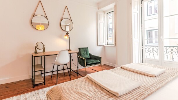 Een slaapkamer met een bed, een bureau, twee stoelen, een spiegel en een raam.