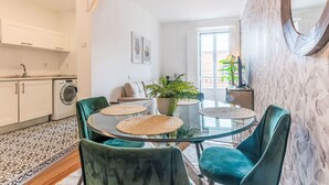 Een moderne keuken met witte kasten, een wasmachine en een eethoek met een ronde tafel en groene stoelen.