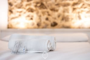 A neatly folded white towel with a visible label on a white surface, possibly a bed or table, against a textured wall. - Maio Apartment – Cozy studio in central Alghero 🌅✨ (Alghero)