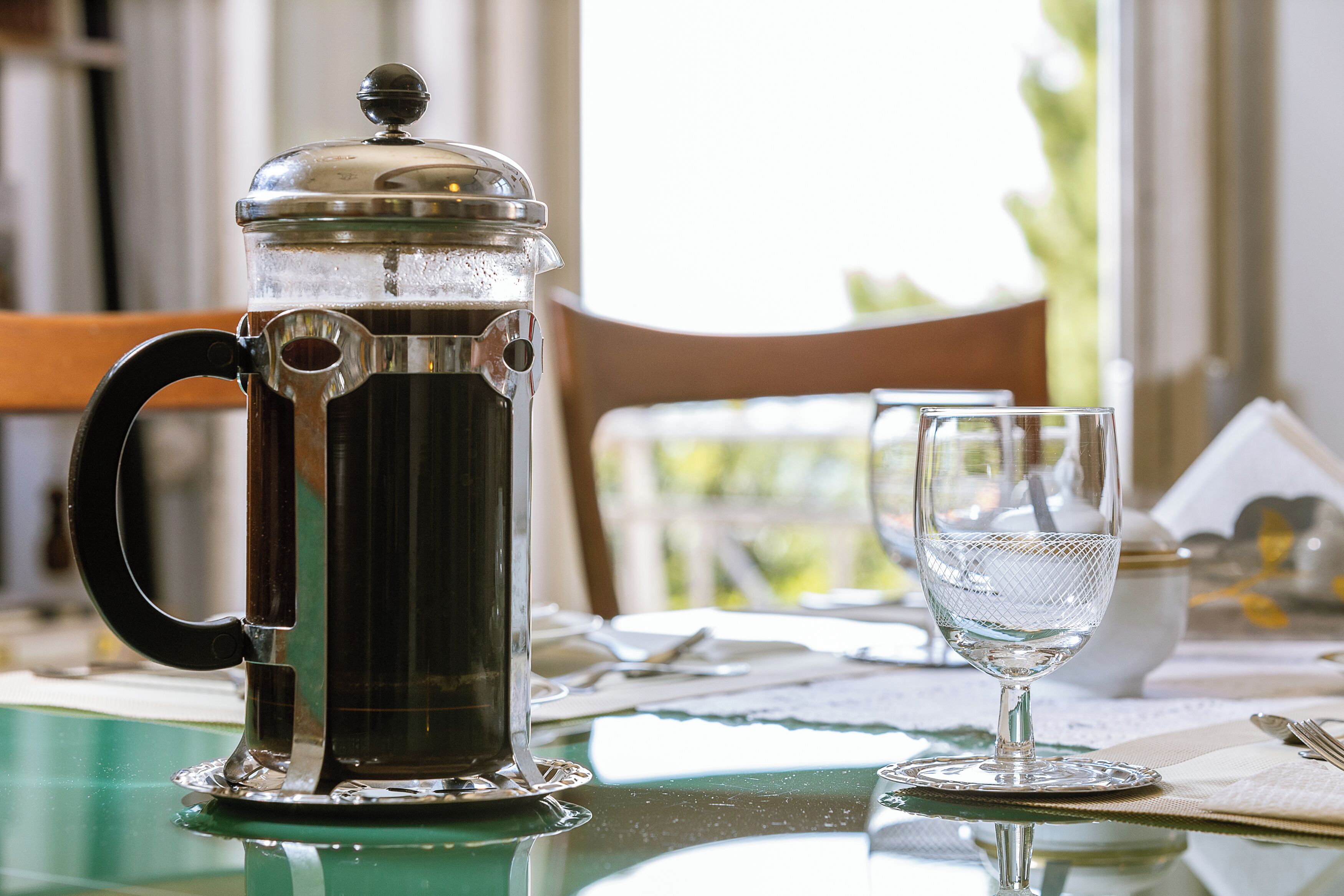 Ein French-Press-Kaffeebereiter und ein Glas auf einem Tisch mit Unterlage.