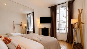 Ein Hotelzimmer mit Bett, Fernseher, Kamin und großen Fenstern mit Vorhängen.