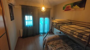 Ein kleines Zimmer mit Etagenbett, einem Schreibtisch, einer Pendelleuchte und einem Fenster mit Vorhängen.