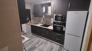 Eine moderne Küche mit dunklen Schränken, einem Edelstahlkühlschrank, einer Mikrowelle und einem Backofen.