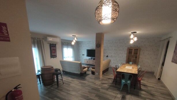 Ein geräumiges Wohnzimmer mit Holzboden, einer Couch, einem Esstisch mit Stühlen, einem Fernseher und einer Pendelleuchte.