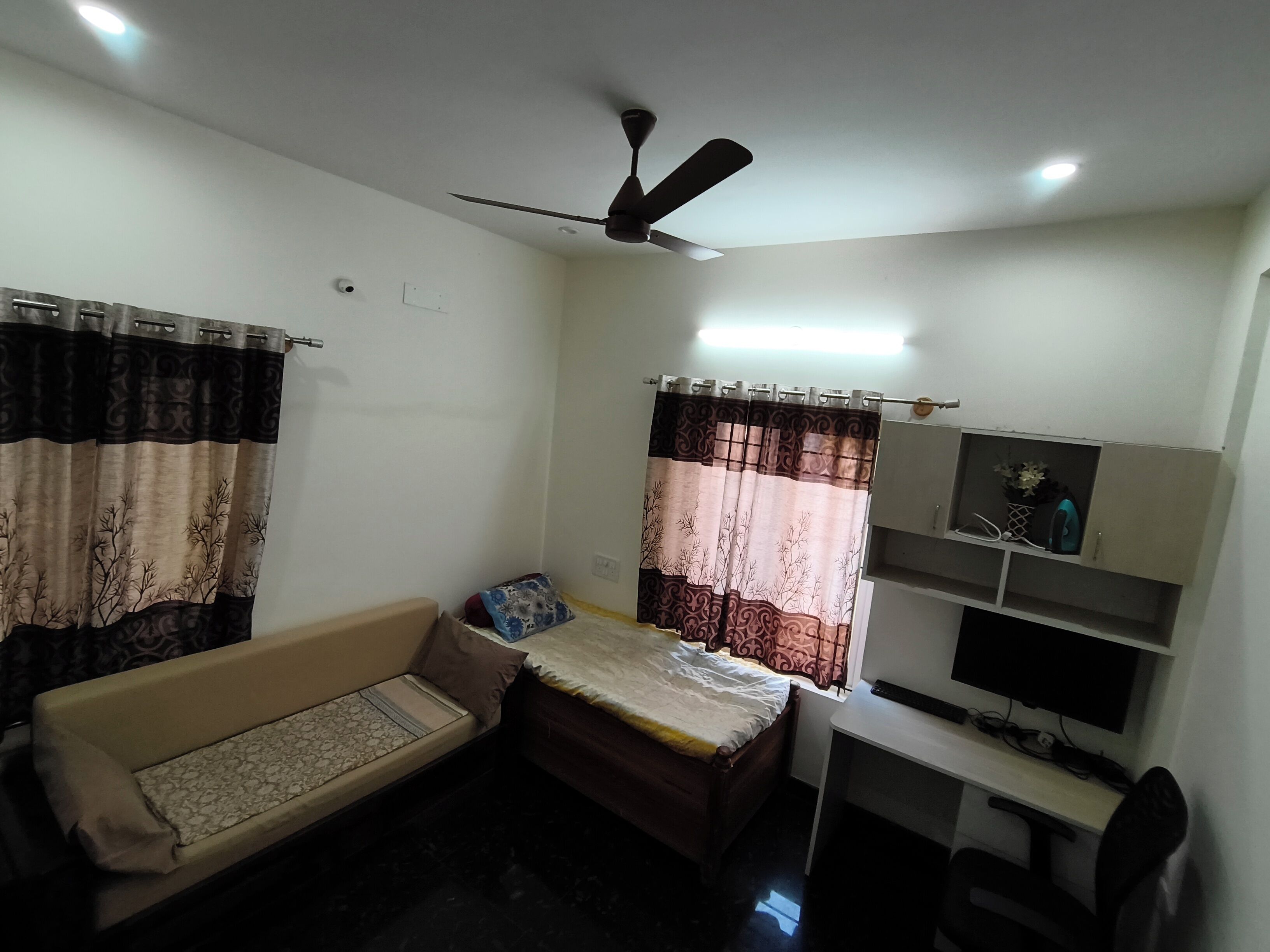 Un dormitorio pequeño con cama, sofá, escritorio y ventilador de techo.