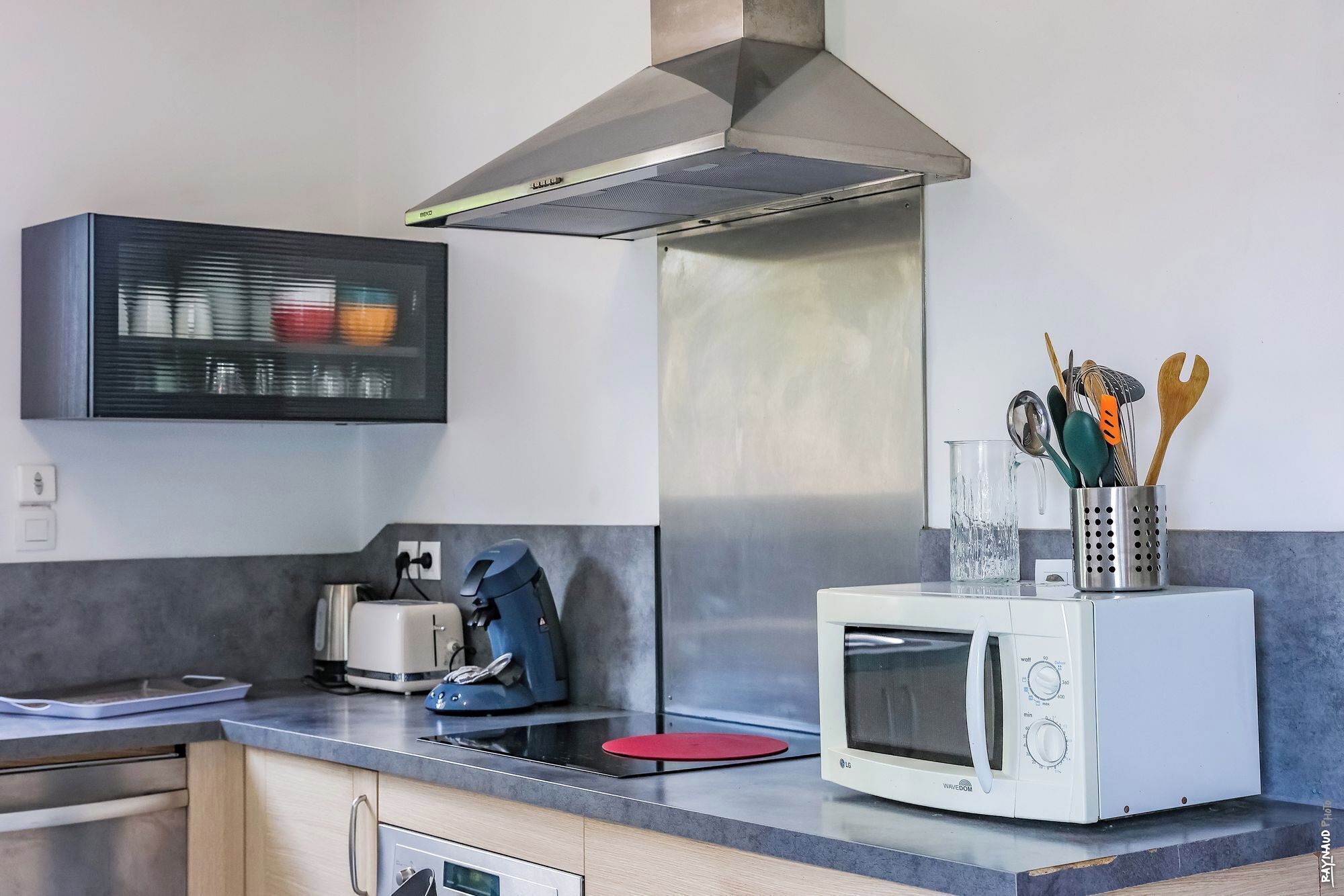 A kitchen with a microwave, toaster, kettle, and a stainless steel range hood.