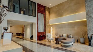 A spacious lobby with a high ceiling, a seating area with sofas and chairs, a reception desk, and a large window. - The Scenic Hotel  (Phnom Penh)