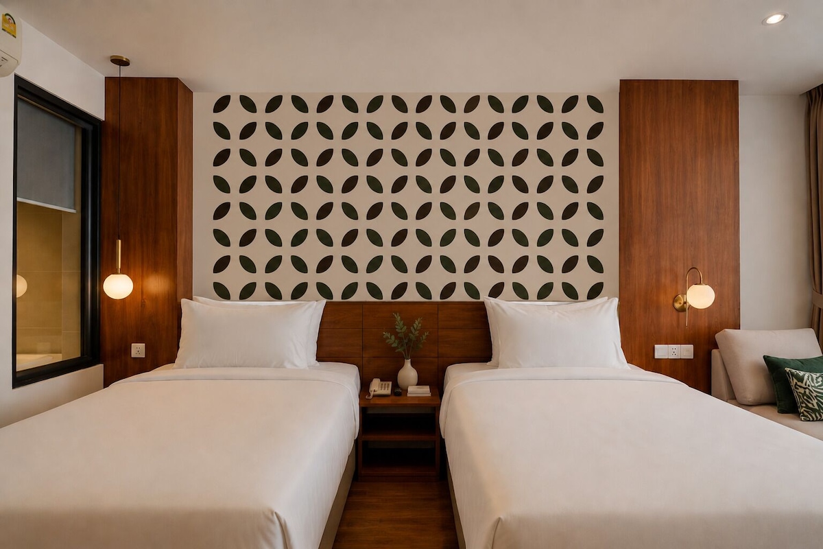 A hotel room with two beds, a wooden headboard, a patterned wall, bedside lamps, and a small table with a vase.