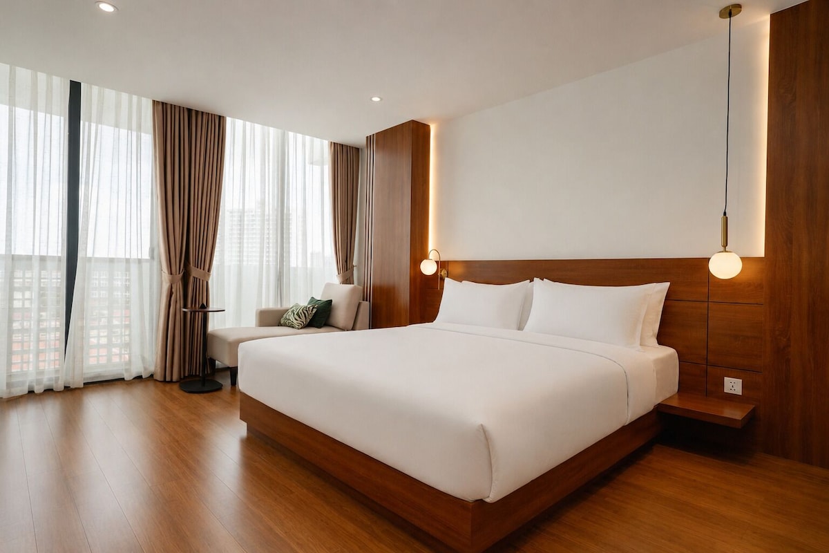 A modern hotel room with a large bed, a sitting area, and a view of the city.