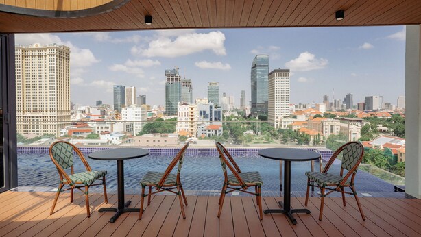A balcony with a city view, wooden flooring, and two round tables with chairs. - The Scenic Hotel  (Phnom Penh)