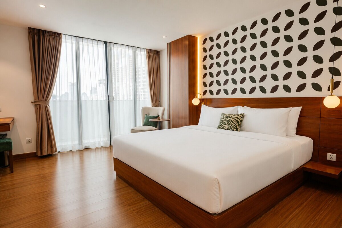 A hotel room with a large bed, a chair, a desk, and a city view through the windows.