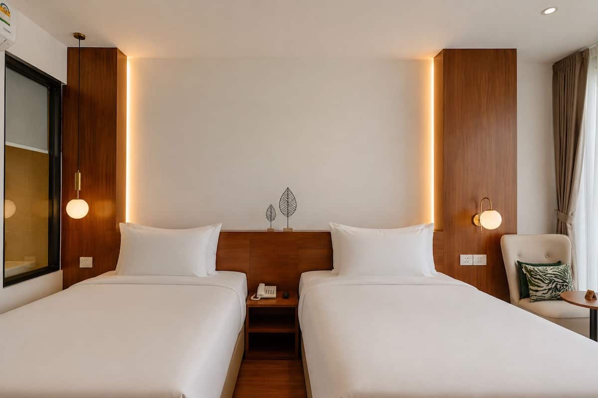 A hotel room with two beds, a wooden headboard, bedside lamps, a small table with a chair, and a mirror.