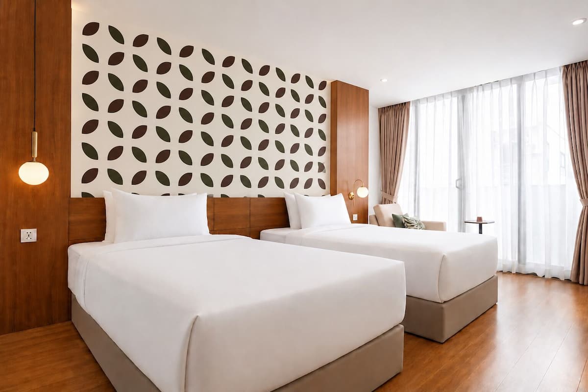 A hotel room with two beds, a patterned wall, and a large window with curtains.
