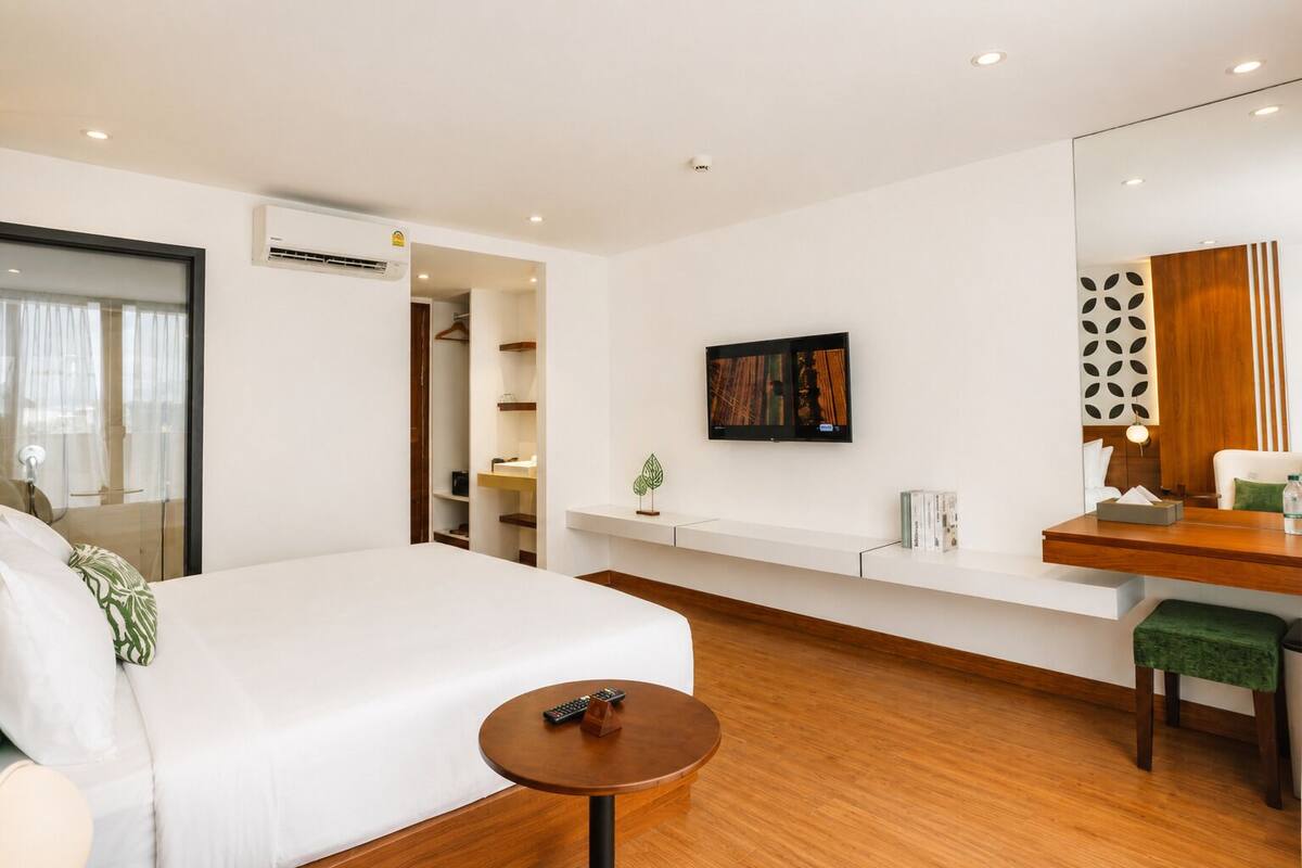 A modern hotel room with a large bed, a small desk, a TV, and a walk-in closet.