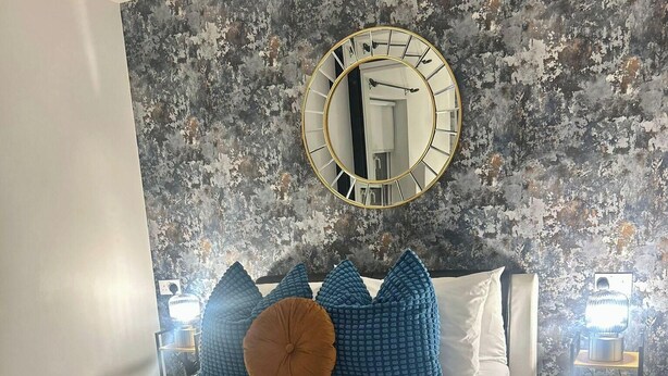 A bedroom with a bed, a round mirror, and a textured wall. - Elegant 2-bed Home - Prime City Centre Location (Leicester)
