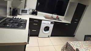A compact kitchen with a stove, microwave, and washing machine. - Elegant 2-bed Home - Prime City Centre Location (Leicester)