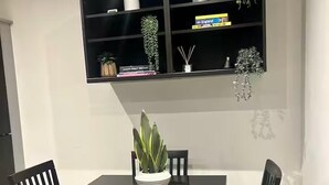 A dining area with a dark wooden table and four chairs. Above the table, there is a black shelf with decorative items and books. - Elegant 2-bed Home - Prime City Centre Location (Leicester)
