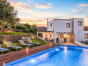 Ein modernes Haus mit Swimmingpool, Sitzgelegenheiten im Freien und einer Steinmauer.