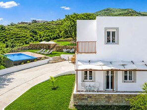 Eine moderne Villa mit Pool, Sitzgelegenheiten im Freien und Blick auf einen üppigen Hügelhang.