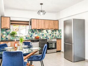 Una cocina moderna con armarios de madera, un refrigerador de acero inoxidable y un comedor con sillas azules.