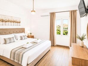 Ein Hotelzimmer mit Bett, Nachttisch, Fernseher, einem Fenster mit Vorhängen und Blick ins Freie.