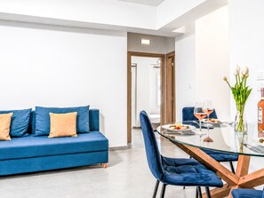 Una sala de estar moderna con un sofá azul, una mesa de comedor de cristal y un florero con flores.