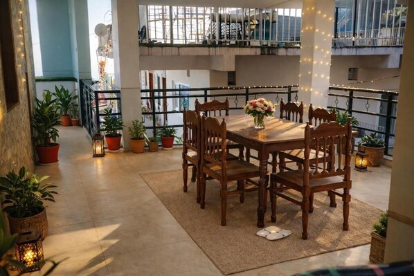 Un espace repas avec une table et des chaises en bois, entouré de plantes en pot et illuminé de guirlandes lumineuses.