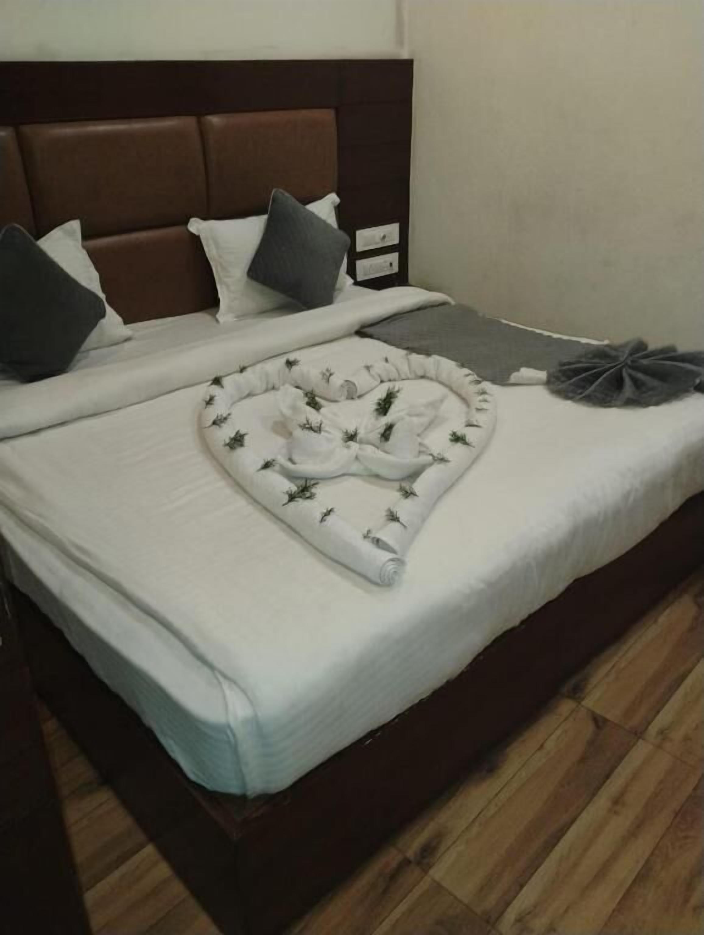 A neatly made bed with a white comforter, a decorative pillow, and a folded blanket on a wooden floor.