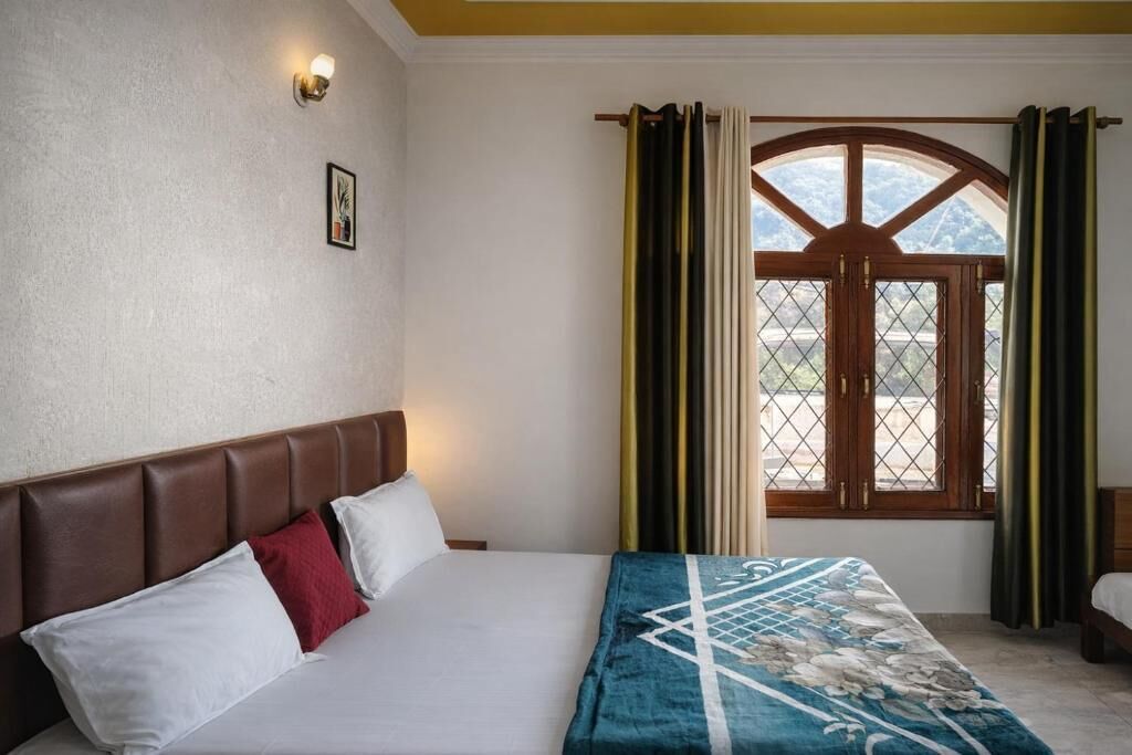 Habitación de hotel con cama, cabecera, ventana con cortinas y lámpara de pared.