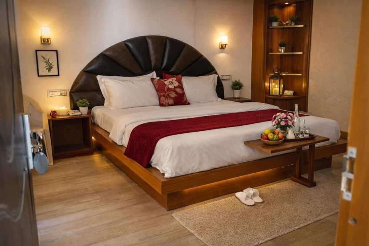 Ein modernes Schlafzimmer mit einem großen Bett, Nachttischen, einer Nachttischlampe, einem Holzregal mit Dekoration und einem kleinen Tisch mit Obstschale und Blumen.
