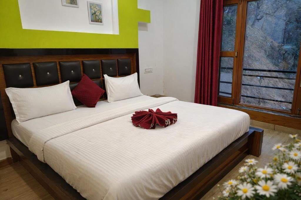 A neatly made bed with white bedding and a red towel, a wooden headboard, and a window with red curtains.
