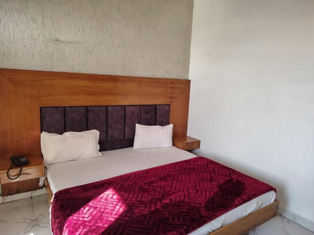 Ein Schlafzimmer mit einem hölzernen Kopfende, zwei weißen Kissen, einer roten, gemusterten Bettdecke und einem Nachttischtelefon.