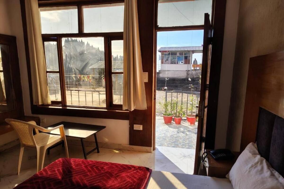 Ein Schlafzimmer mit Bett, Schreibtisch und Stuhl. Ein Balkon mit Blumentöpfen und Blick auf ein Gebäude.